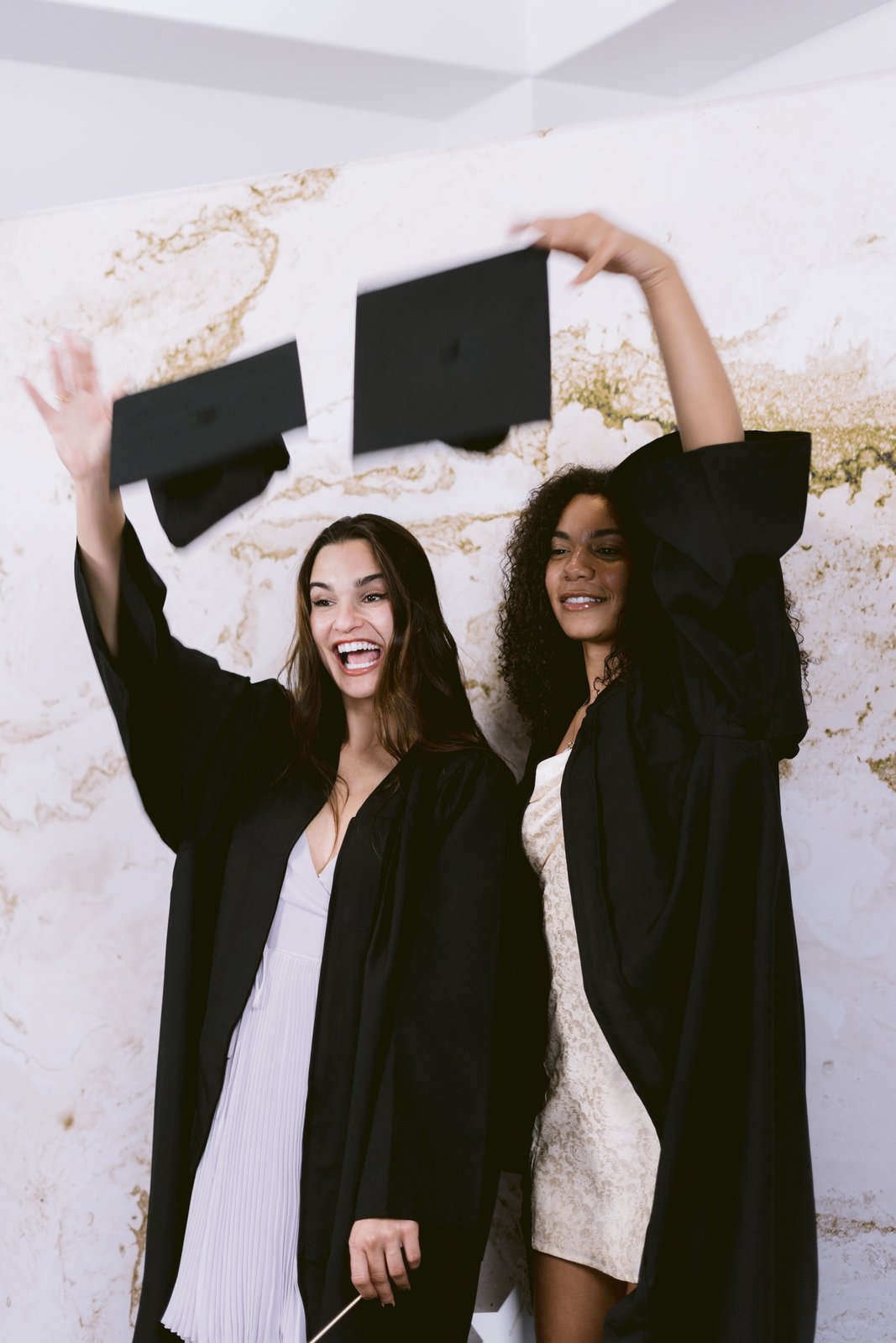 Two graduates throwing their caps in the air in front of the booth backdrop